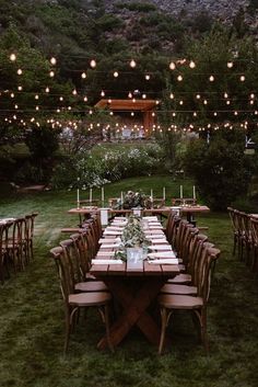 an outdoor dinner table set up with candles and greenery on the lawn, surrounded by string lights