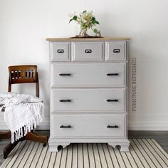 a white dresser sitting next to a wooden chair in a room with a striped rug on the floor