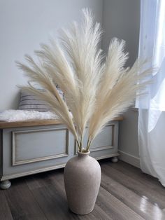 a vase with some white flowers in it on a wooden floor next to a window