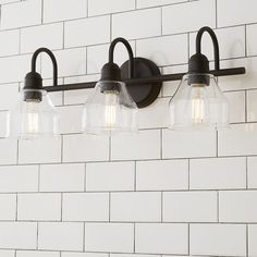 three lights are hanging on the wall in front of a white brick wall with black fixtures