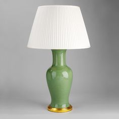 a green table lamp with a white shade on the top and gold trim around the base