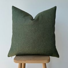 a dark green pillow sitting on top of a wooden chair next to a white wall