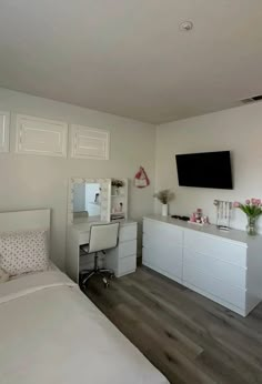 a bedroom with white furniture and a flat screen tv mounted on the wall above it