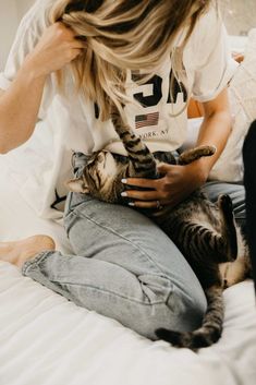 a woman sitting on top of a bed holding a cat