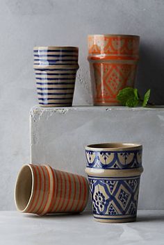 three ceramic cups sitting next to each other on top of a shelf with plants in them