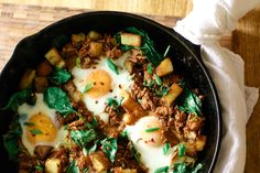 an iron skillet filled with eggs, meat and spinach on top of a wooden table