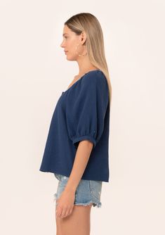 A navy blue bohemian puff sleeve blouse designed in soft cotton gauze. Cotton gauze Relaxed fit Short raglan puff sleeve Round neckline with contrast thread detail Button front Bohemian summer blouse A contrast thread detail adds a unique charm to this classic bohemian blouse. Designed in soft cotton gauze, featuring raglan puff sleeves, a flattering scooped neckline, and a button front. Model is 5'9, wearing a size S.Style: I-15055W-RJZ Navy Short Sleeve Blouse For Summer, Blue Top With Gathered Short Sleeves, Summer Balloon Sleeve Peasant Top For Daywear, Spring Short Sleeve Cotton Gauze Tops, Spring Cotton Gauze Short Sleeve Tops, Cotton Peasant Top With Puff Sleeves, Summer Cotton Gauze Blouse For Daywear, Summer Peasant Tops With Balloon Sleeves, Peasant Top With Balloon Sleeves For Summer