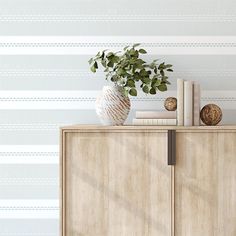 a white vase sitting on top of a wooden cabinet next to books and a plant