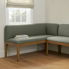 a corner bench with a book on it in front of a window and wooden floor