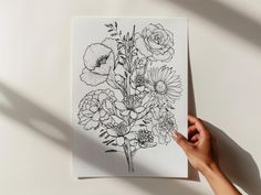 a person holding up a piece of paper with flowers drawn on it in black ink