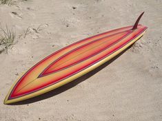 a red and yellow surfboard laying in the sand