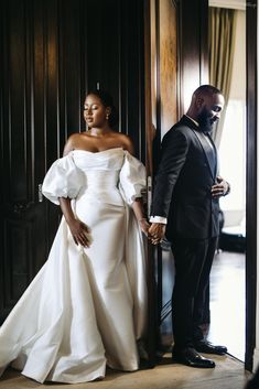 a man and woman standing next to each other in front of a door holding hands