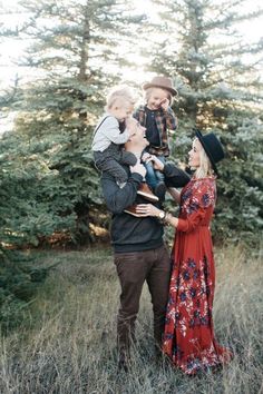 a man and woman holding two children in their arms while standing in tall grass with trees behind them