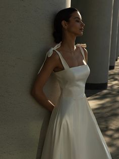 a woman in a white dress leaning against a wall