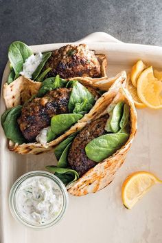 three tacos with spinach and lemon wedges on a white platter next to a small jar of yogurt