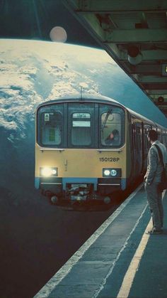 a man standing next to a train at a station with the earth in the background