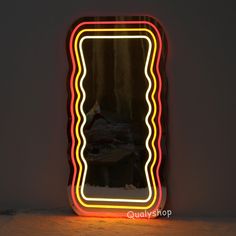 a mirror that is lit up in the shape of a rectangle with an image of a woman sitting on a bed