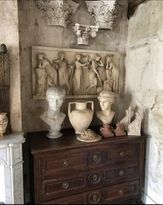 an old dresser with vases and busturines on it in a room filled with statues