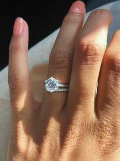 a woman's hand with a diamond ring on her left hand and the other hand holding an engagement ring