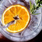 an orange cut in half sitting on top of a glass bowl filled with ice and rosemary