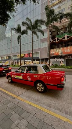 a red taxi cab driving down a street next to tall buildings with palm trees in the background