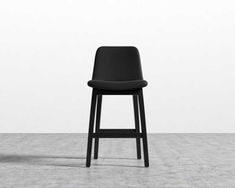 a black stool sitting on top of a cement floor next to a white wall in an empty room