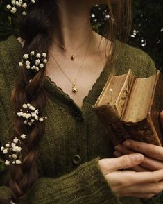 a woman with long hair holding an open book in her hands and flowers around her neck