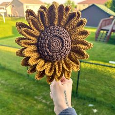 a person holding up a crocheted sunflower in front of a grassy field