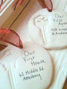 two white cookies with red ribbon on top of each one and the words our first house are written on them