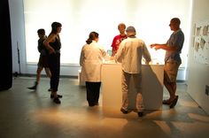 a group of people standing around in front of a white wall with pictures on it