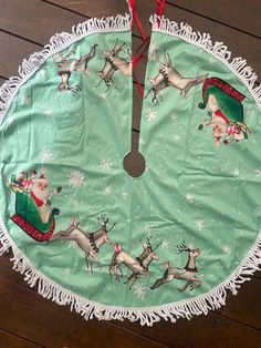 a green christmas tree skirt with santa claus and reindeers on it, sitting on a wooden floor