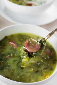 a spoonful of soup with spinach and other vegetables in white bowls on a table