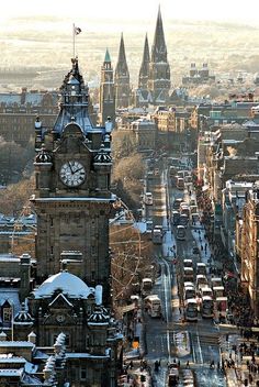 a large clock tower towering over a city filled with tall buildings and snow covered streets