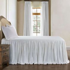 a white bed sitting in a bedroom next to a window with drapes on it