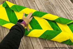 a person is holding onto a green and yellow blanket on a wooden floor with their hand