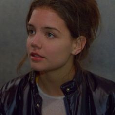 a young woman wearing a leather jacket looking at the camera while standing in front of a wall