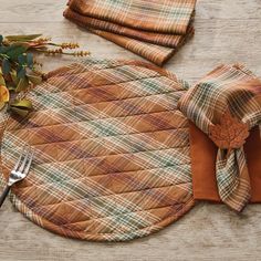 an orange plaid placemat and two napkins on a wooden table with silverware