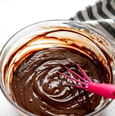 a glass bowl filled with melted chocolate on top of a white countertop next to a pink whisk