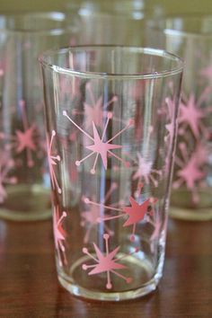 four glasses with pink and white designs are sitting on a wooden table, one is empty