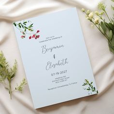 the wedding stationery is laid out on a bed with flowers and greenery around it