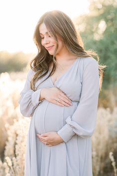 a pregnant woman standing in a field with her hands on her stomach