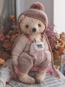 a stuffed teddy bear wearing a hat and overalls sitting on top of a pillow