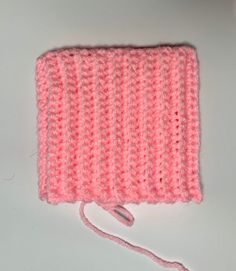 a pink crocheted square with a white string on the end and a hook in the middle