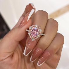 a woman's hand holding a ring with a pink diamond in the center and two diamonds around it