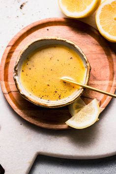 a wooden plate topped with a bowl of soup and sliced lemons next to it