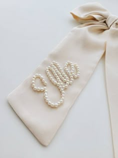 a white tie with pearls on it and a monogrammed bow at the end