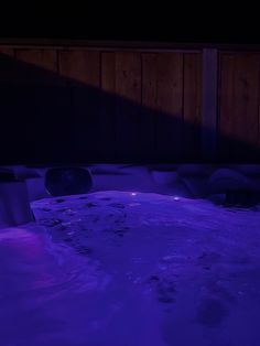 a hot tub in the middle of a room with purple lights on it and water running down the side