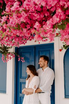 a man and woman standing in front of a blue door with pink flowers on it