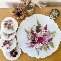 four plates with flowers on them sitting on a table next to a potted plant