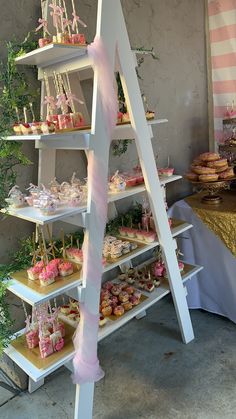 a table topped with lots of cakes and cupcakes next to a tall white ladder